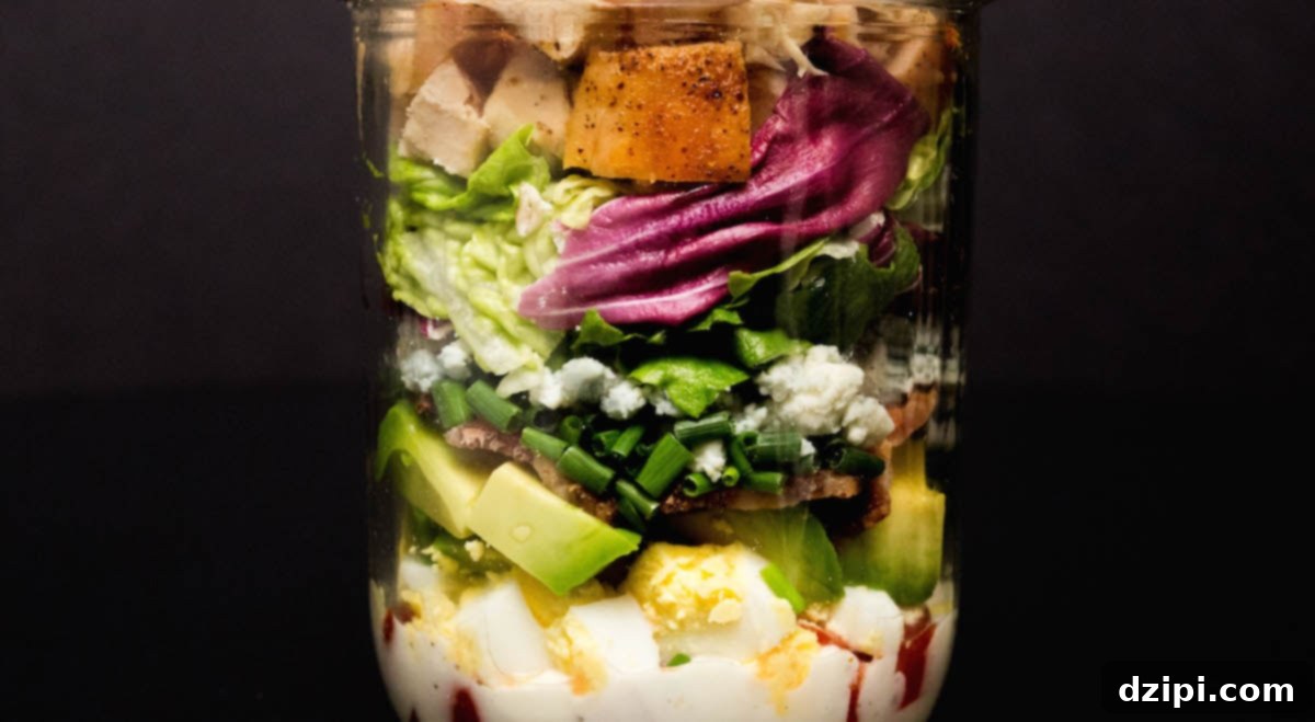 Ultimate Mason Jar Cobb Salad 2 A mason jar filled with vibrant Cobb Salad layers on a dark background.