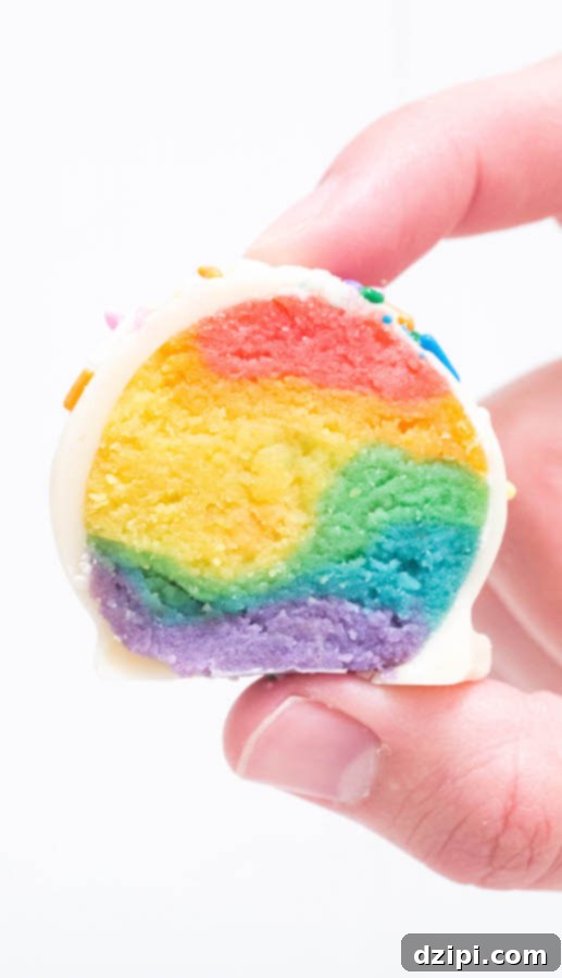 Whimsical Rainbow Cake Truffles 4 A close-up shot of a hand holding a perfectly halved Rainbow Cake Truffle, showcasing its colorful interior layers.