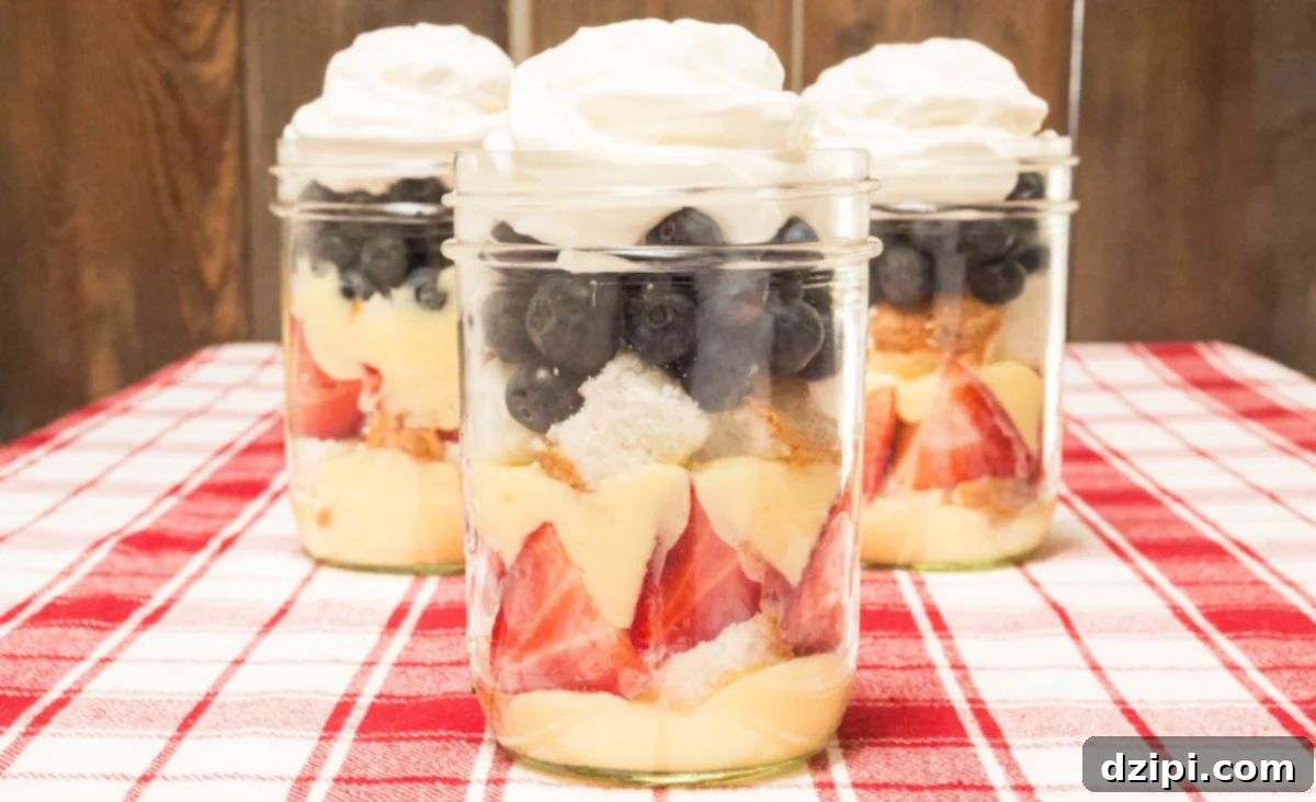 Three mason jars filled with layers of angel food cake, strawberries, blueberries, pudding, and whipped cream, creating a vibrant red, white, and blue dessert for July 4th.
