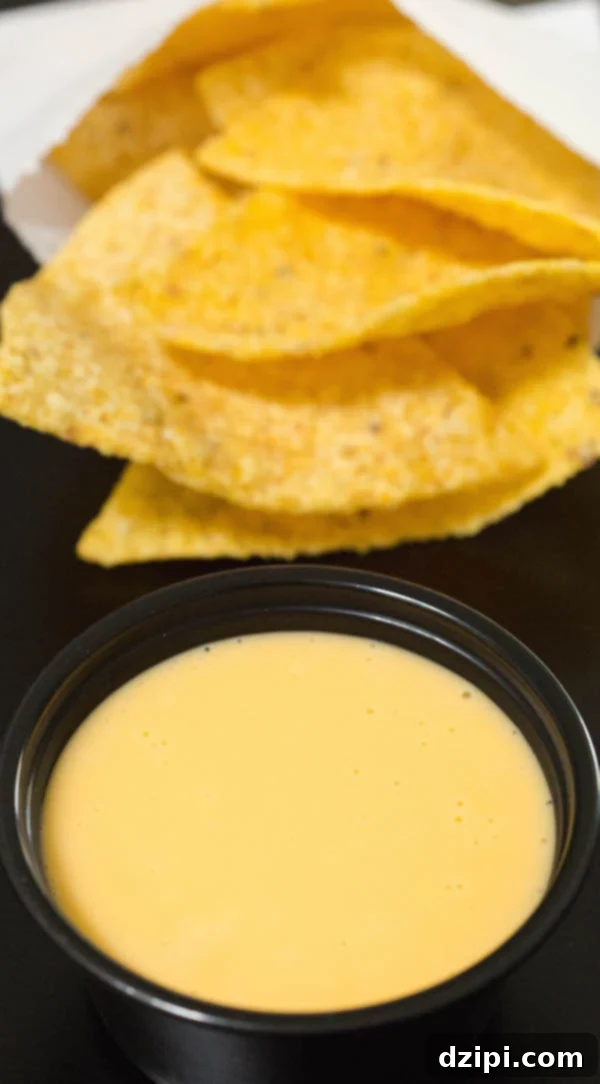 A small black cup of homemade Taco Bell Nacho Cheese in front of a bag of tortilla chips.