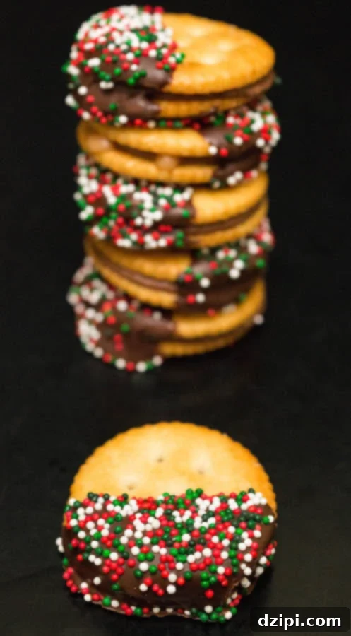 A close-up view of a single chocolate-dipped Rolo Ritz Christmas Cracker, positioned in front of a inviting stack of more festive treats.