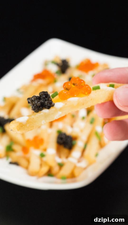 A hand holds up a single golden French fry, elegantly topped with contrasting black and orange caviar and fresh green chives.