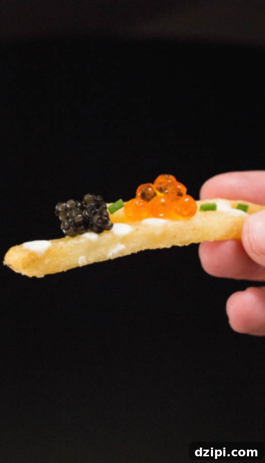 Close-up of a single French fry, showcasing distinct black caviar and vibrant orange salmon roe pearls on its crisp surface.