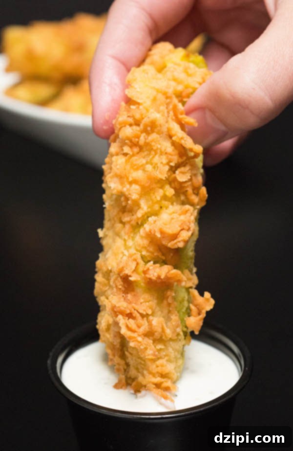 A golden-brown Chicken Fried Pickle being perfectly dipped in creamy ranch sauce.
