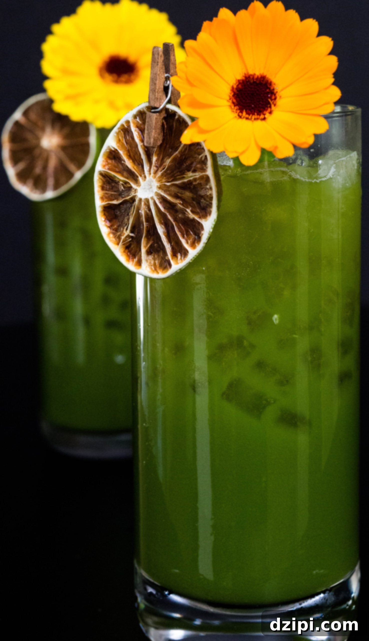 Two highball glasses filled with Green Juice Margaritas garnished with edible flowers and lime wheels. A healthy cocktail.