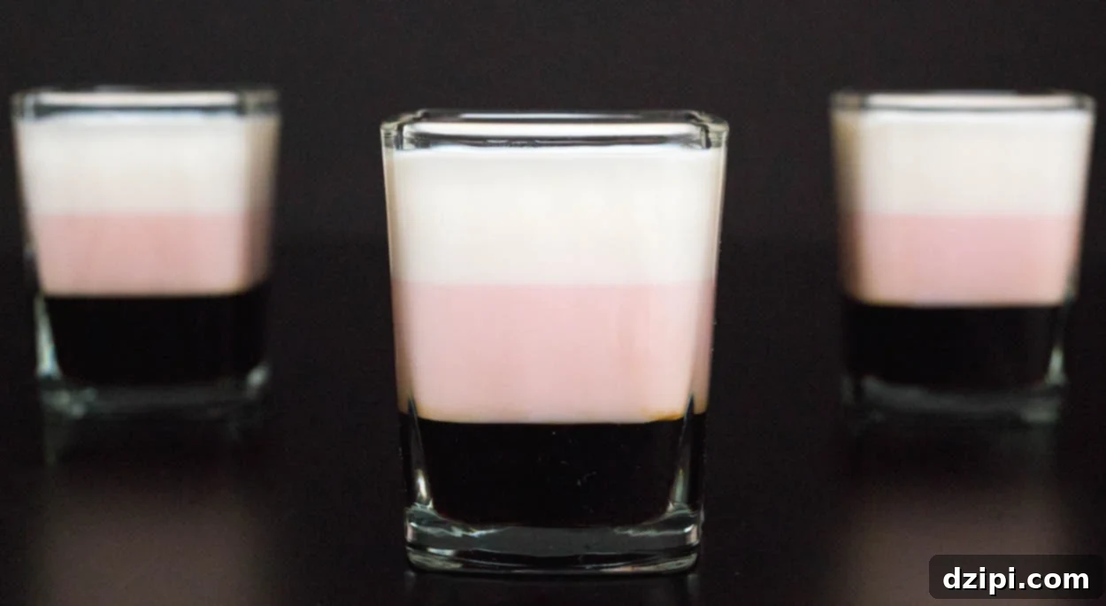 Three layered Neapolitan Shots in square shot glasses on a black background.