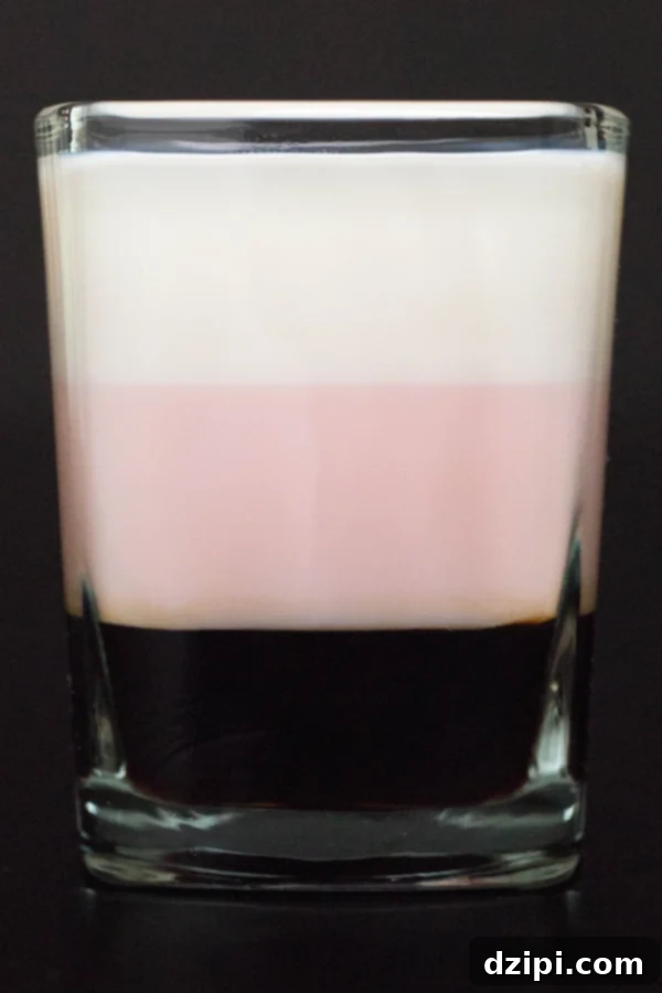Close up of a Neapolitan Shot featuring a dark brown layer, a pink layer, and a white layer.