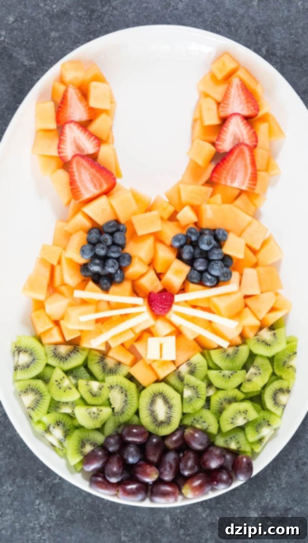 An adorable Easter bunny shaped fruit tray featuring slices of cantaloupe, kiwi, grapes, blueberries, and strawberries, perfect for a spring celebration.