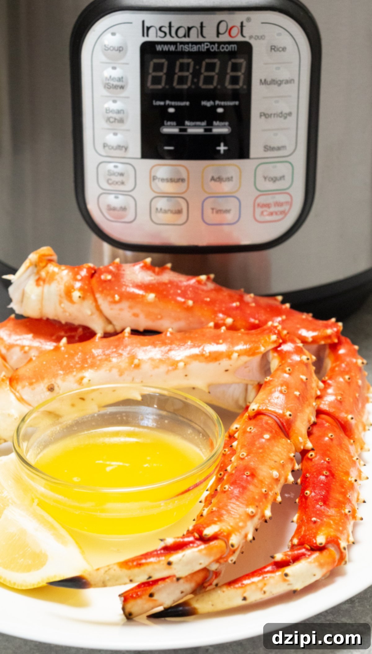 Three cooked crab legs sit on a plate with butter in front of an Instant Pot, ready to be enjoyed.