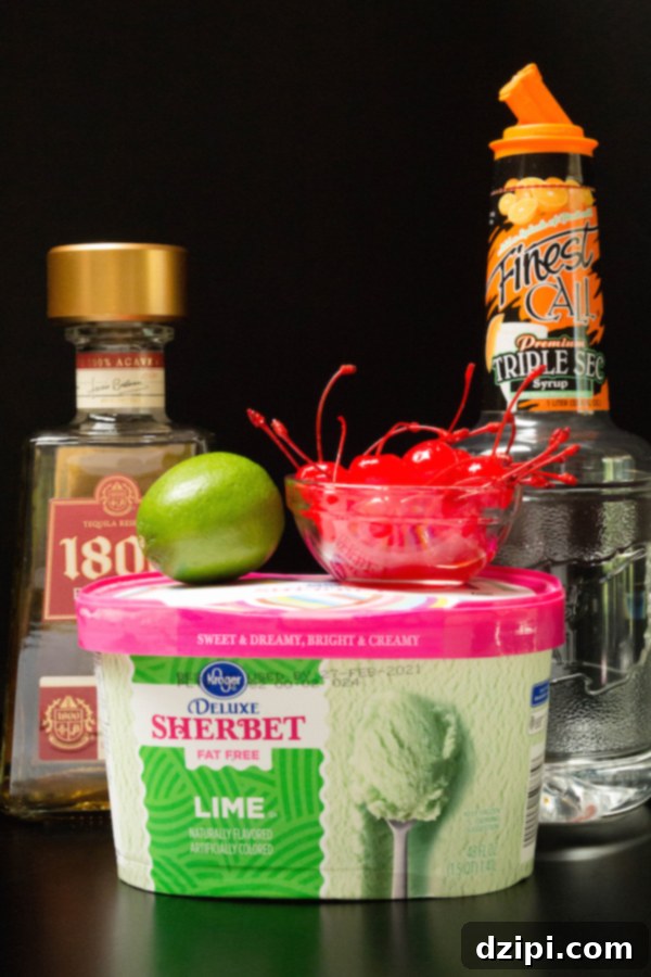 The essential ingredients for crafting Lime Sherbet Margaritas laid out on a dark surface: a tub of vibrant lime sherbet, fresh limes, a bottle of premium tequila, a bottle of triple sec, and bright red maraschino cherries.
