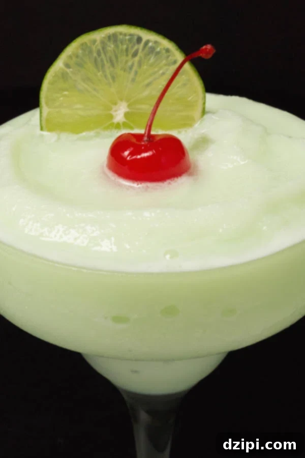 A close-up shot of a Lime Sherbet Margarita, artfully garnished with a vibrant maraschino cherry and a crisp lime slice, all against a dark background.