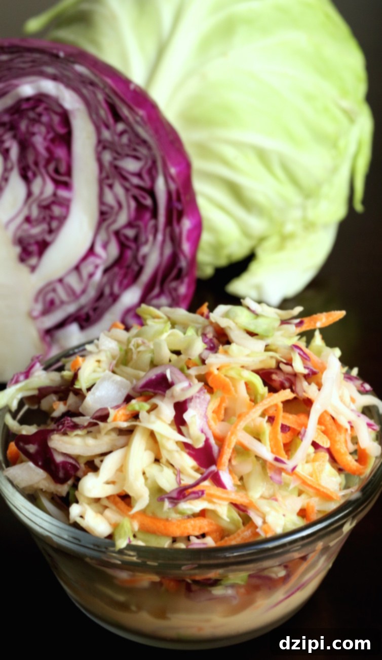 A small glass bowl of copycat KFC coleslaw sits in front of a cabbage head sliced in half.