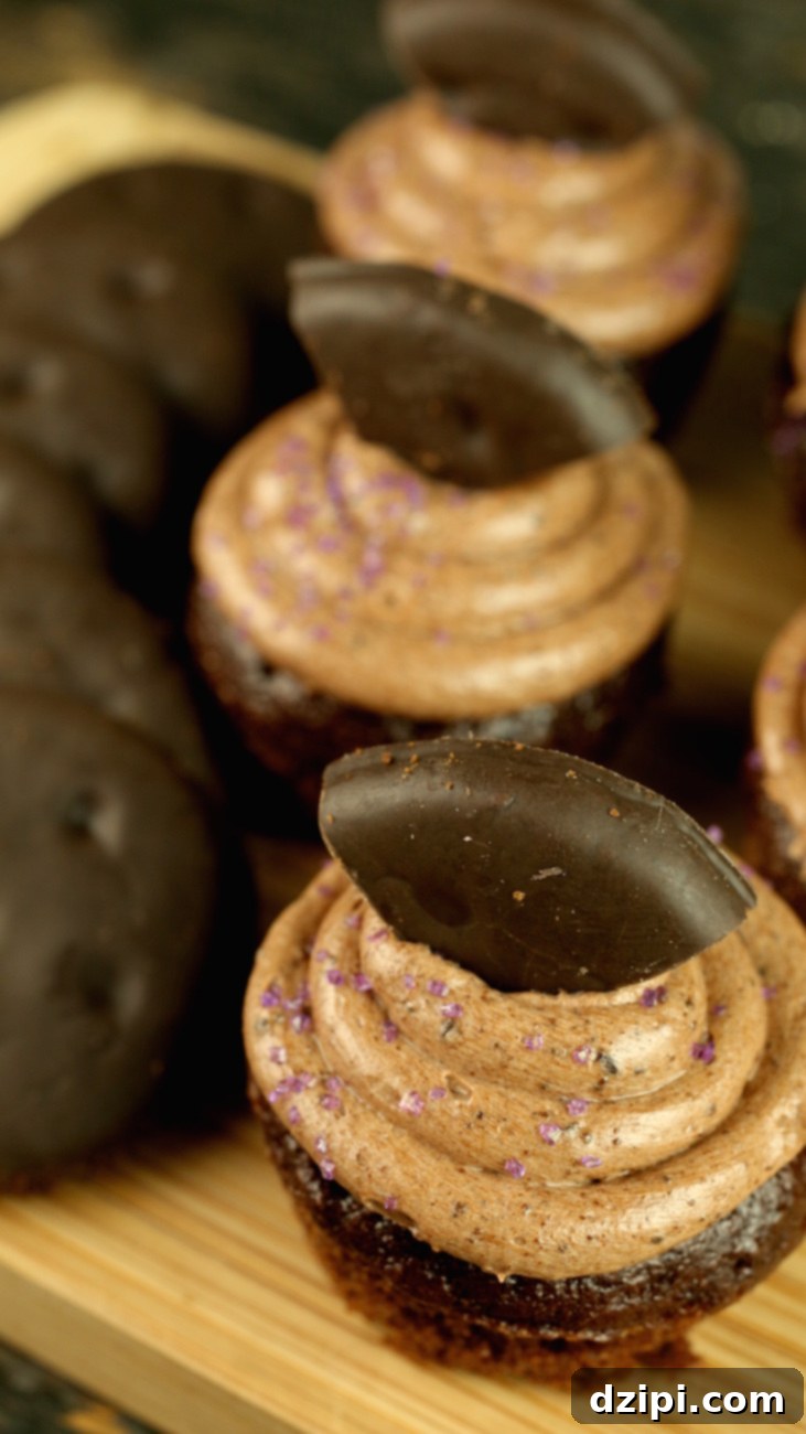 Several small chocolate cupcakes that are garnished with Thin Mint cookies sit on a cutting board, ready to be served.
