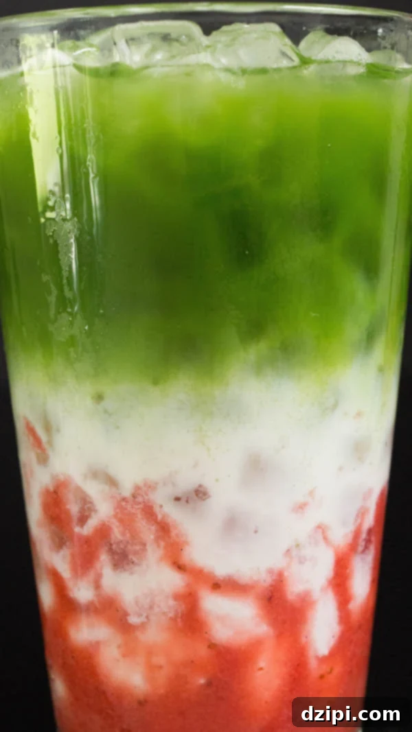 Close-up detailed view of the three distinct layers of strawberry syrup, milk, and vibrant matcha in an iced latte.