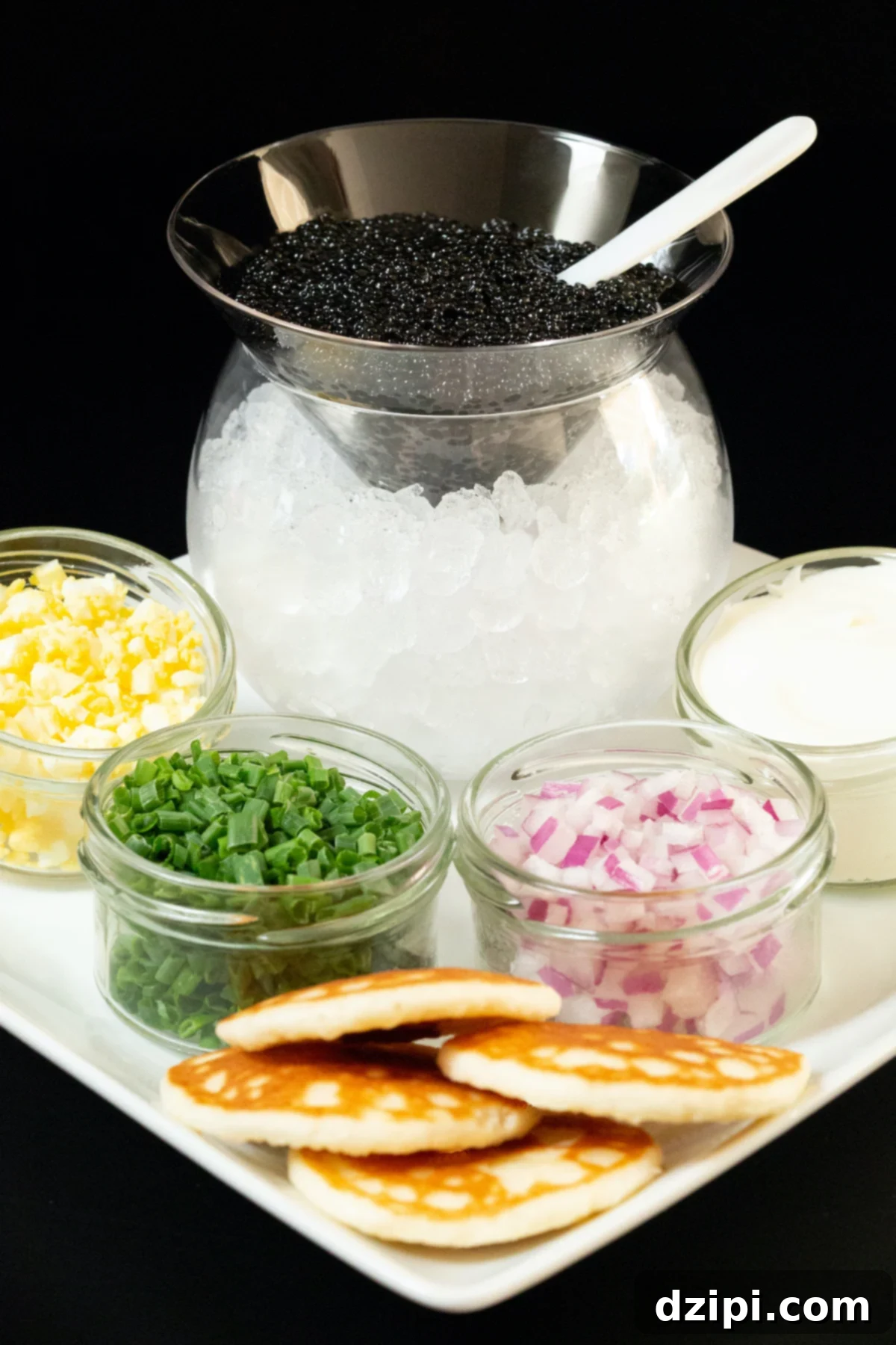Serving Caviar: A Connoisseur's Guide 2 Classic caviar service setup with caviar in a glass cone over ice, surrounded by crème fraîche, chopped onions, hard-boiled egg, and blinis.
