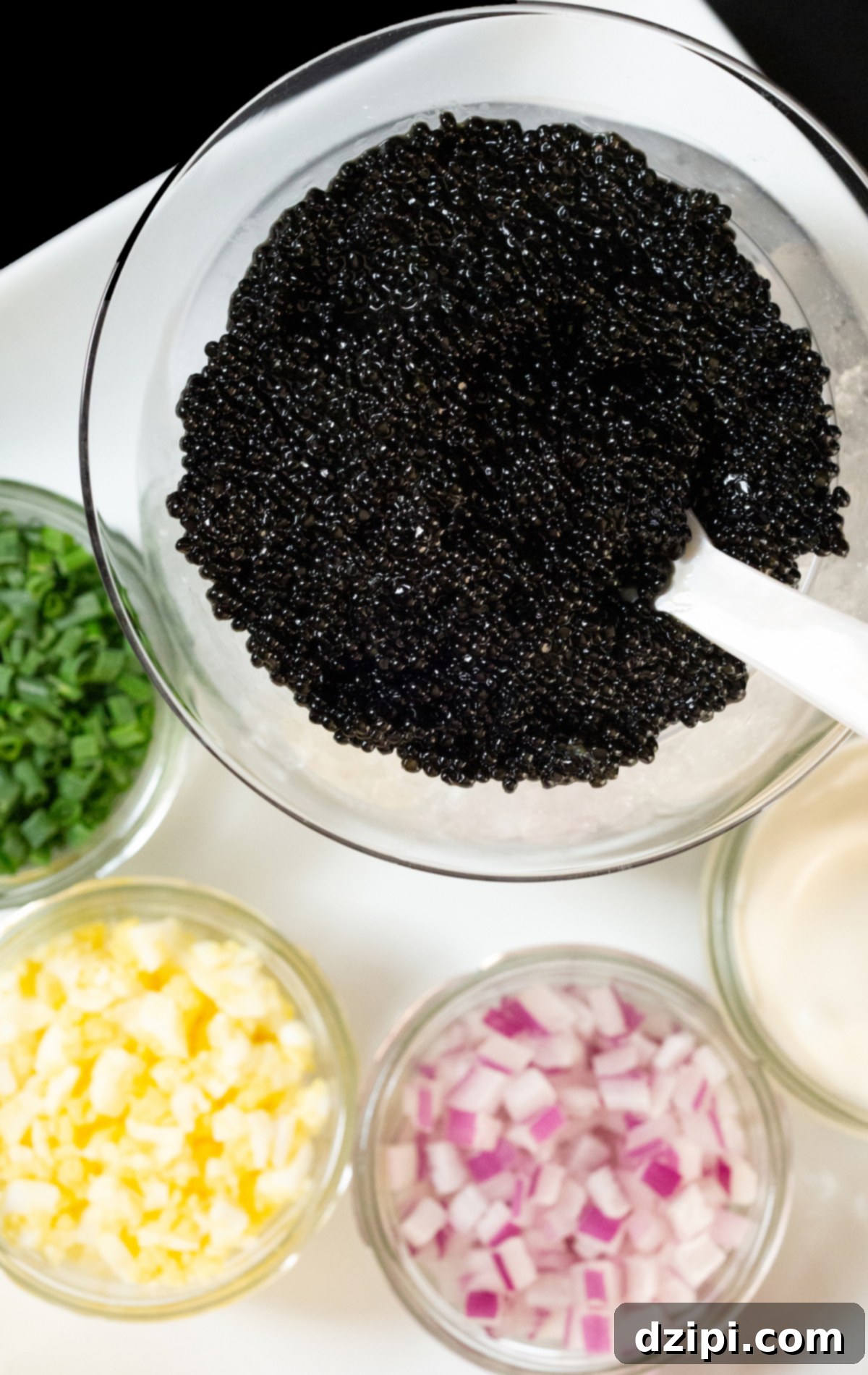 Serving Caviar: A Connoisseur's Guide 3 Overhead view of a caviar bowl with a pearl spoon, surrounded by jars of chopped green onion, red onion, hard-boiled egg, and crème fraîche.