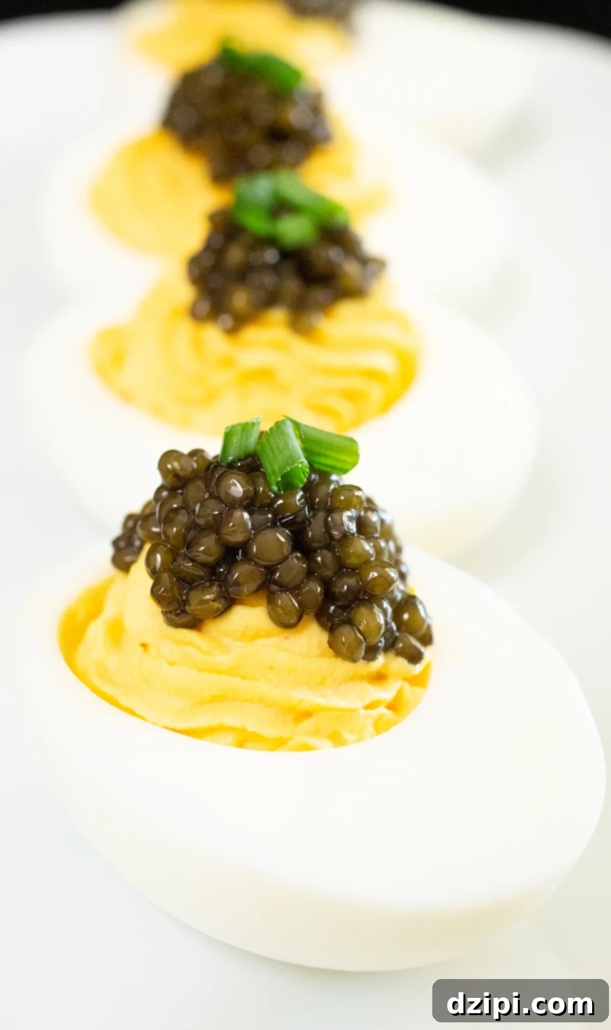 Serving Caviar: A Connoisseur's Guide 4 Four deviled eggs topped with caviar and chives arranged on a white plate.