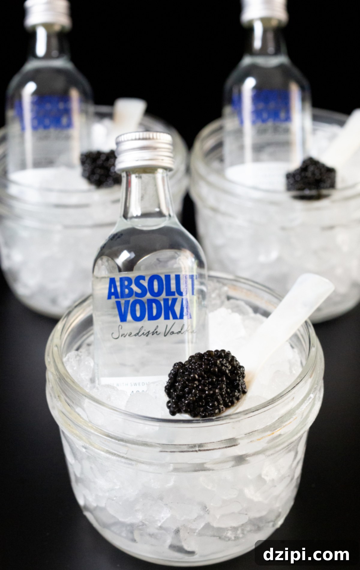 Serving Caviar: A Connoisseur's Guide 7 Three small glass jars filled with pebble ice, each containing a mini vodka bottle and a pearl spoon with caviar.